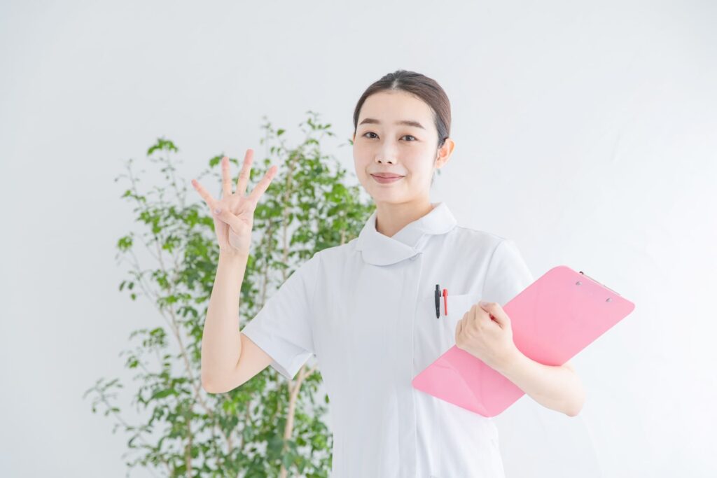 白衣を着た女性医師が指で4のハンドサインをしている写真