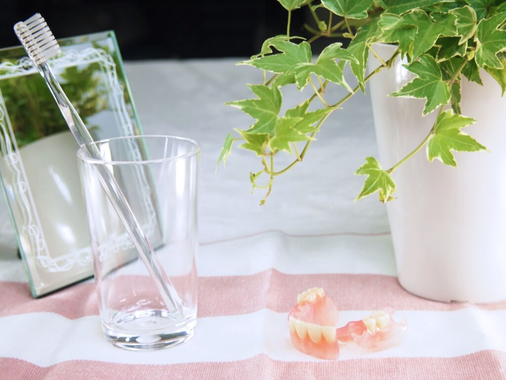 入れ歯と歯ブラシ、コップが並んだ日常的な義歯ケアのイメージ