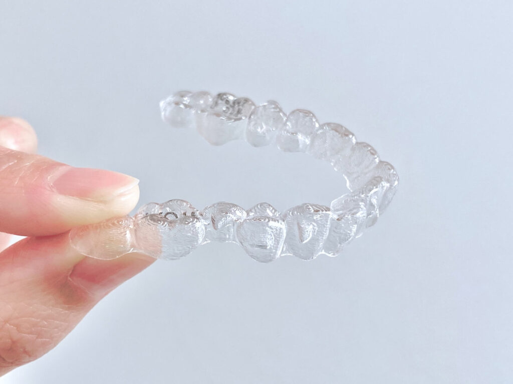 指先で持たれた、装着しても目立ちにくい透明なマウスピース型の矯正装置