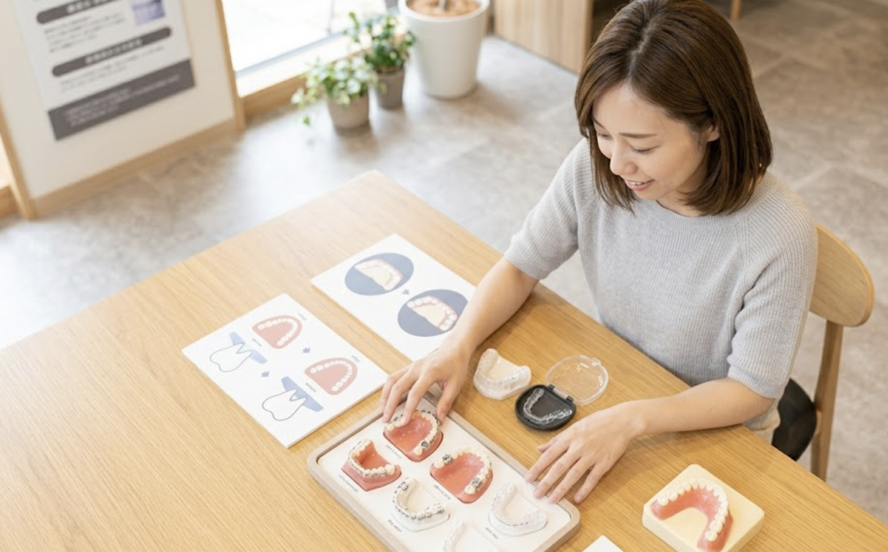 斜め上から俯瞰して、テーブルに並んだ複数の矯正治療肢の模型を能動的に比較する日本人女性の様子