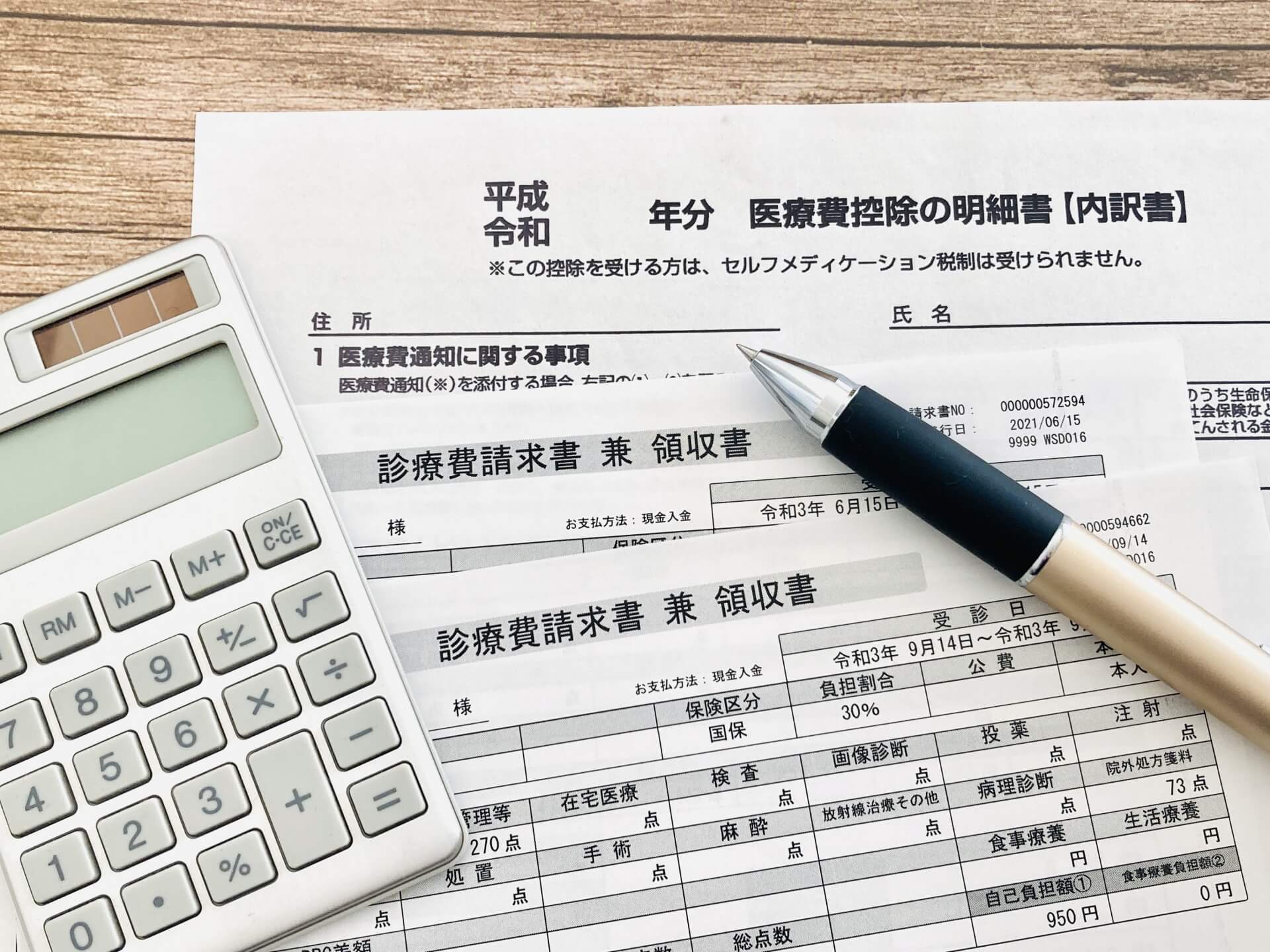 確定申告のための医療費控除明細書と領収書、計算用電卓のクローズアップ
