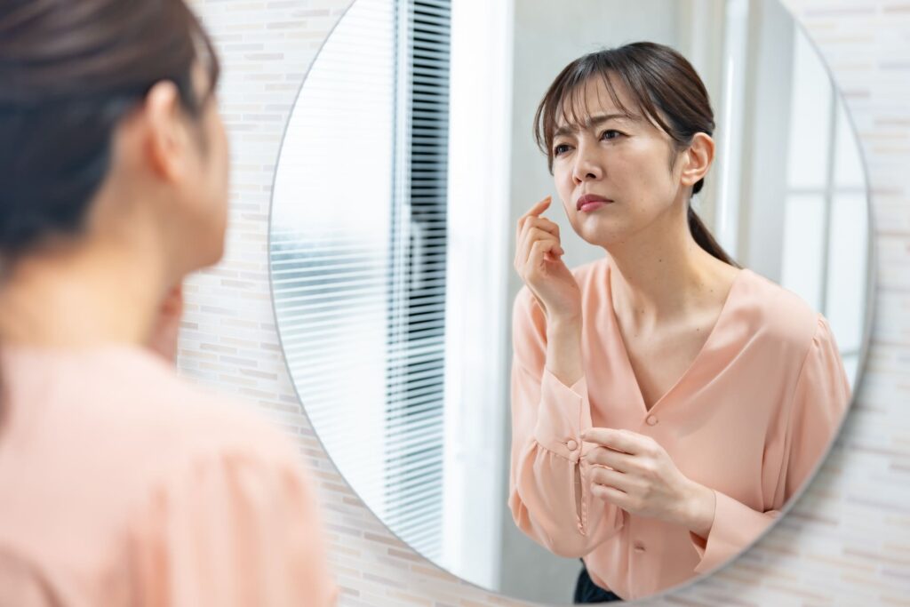 ほうれい線が気になって頬を触れる女性のイメージ
