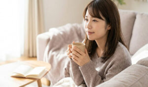 親知らず抜歯後、自宅のソファで温かい飲み物を手にリラックスする日本人女性の様子
