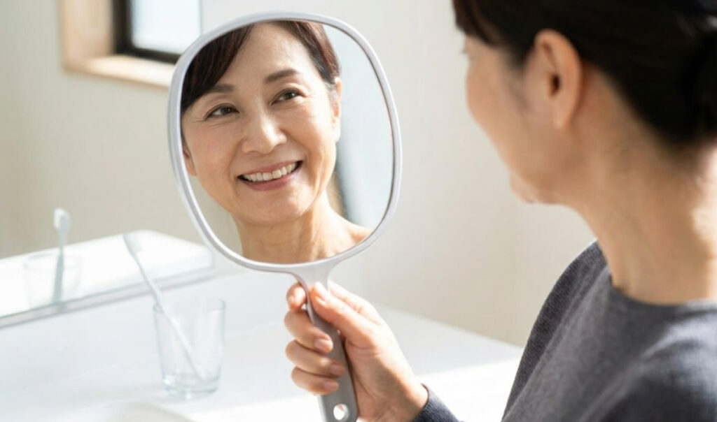 鏡を見て自信を持って微笑む、健康な口元の日本人女性の様子