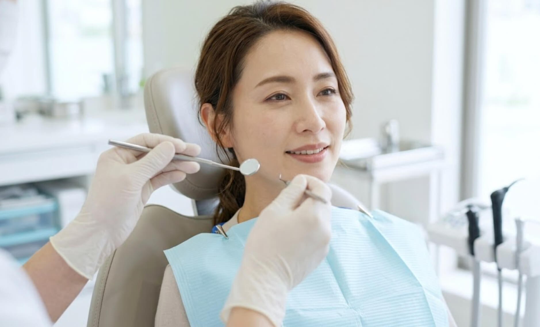 明るい歯科医院で、歯科医師がミラーを使いメンテナンスを行っている最中の、リラックスした40代日本人女性の顔のアップ写真の様子