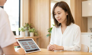 クリニックのカウンセリングルームで、歯科医師からタブレットを使って説明を受け、安心した様子で納得する日本人女性の様子