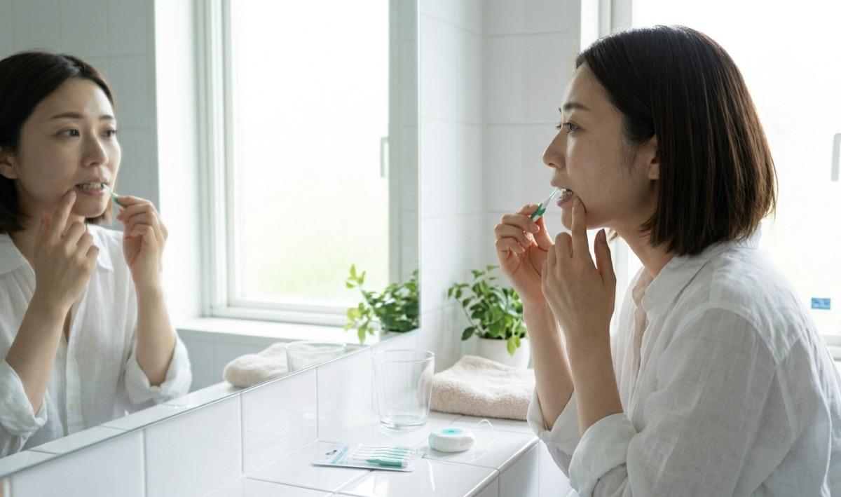 洗面所で歯間ブラシを使ってセルフケアをする女性の様子