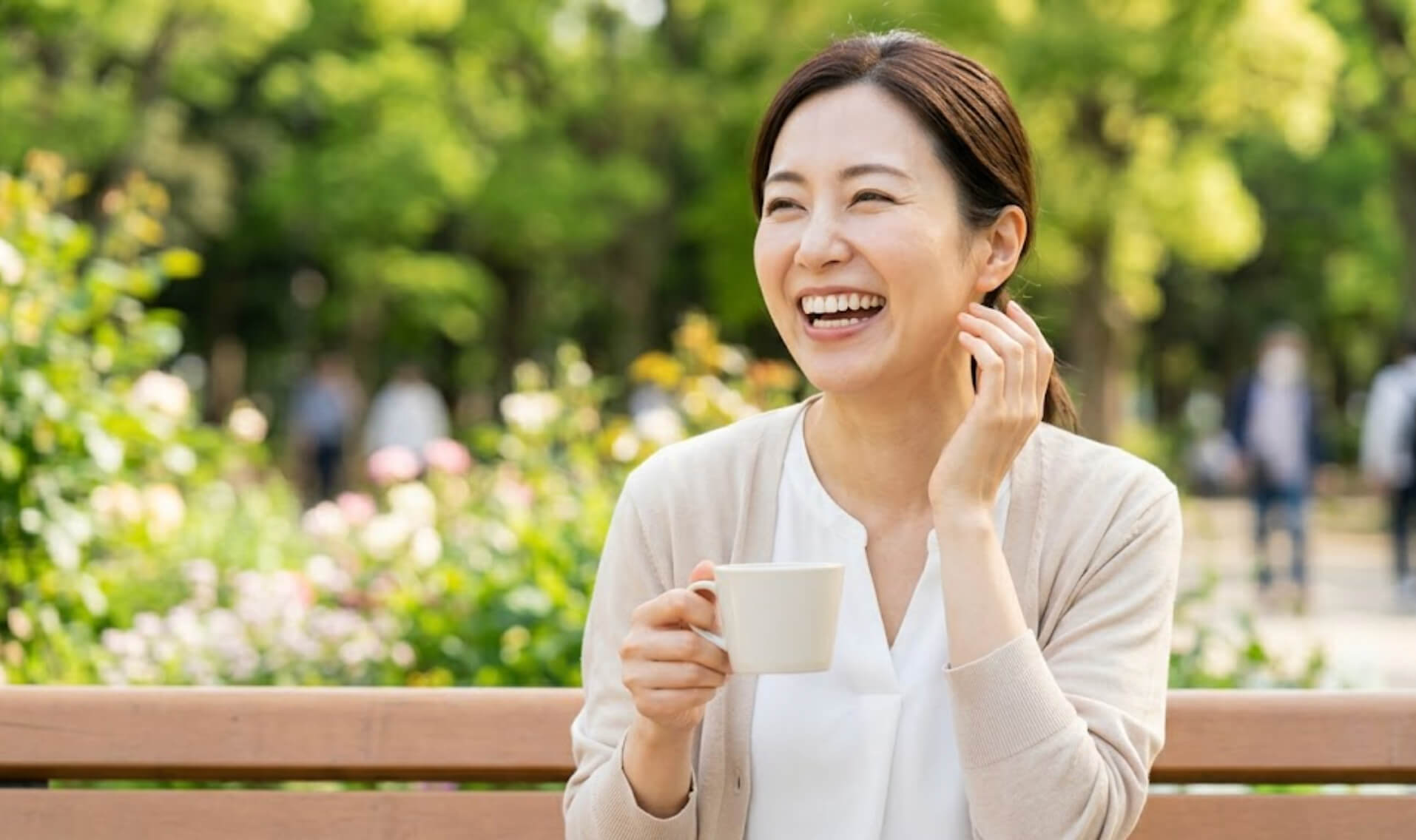 自然光の中でリラックスし、整った歯並びで笑う日本人女性の上半身の様子