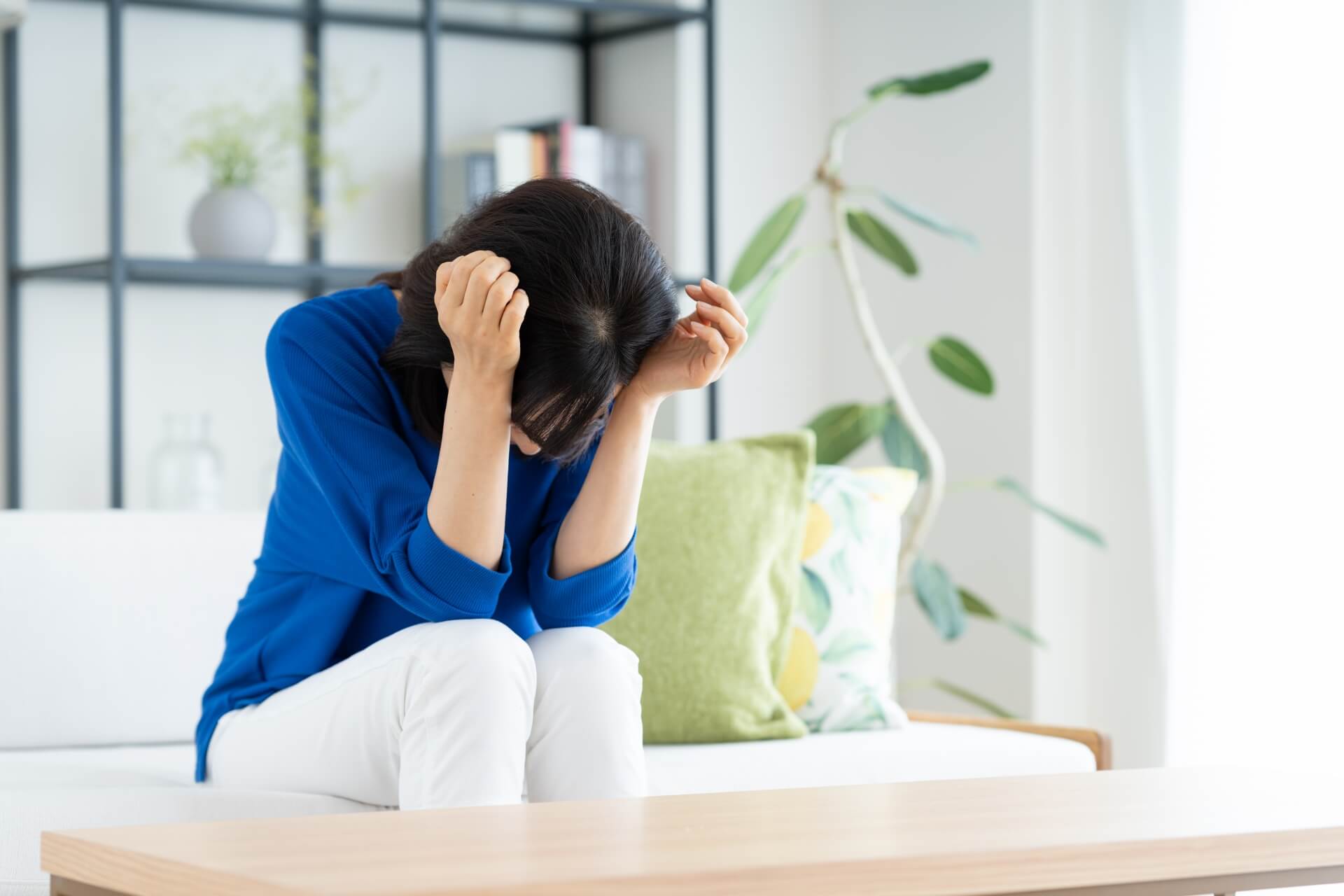 ソファで頭を抱え、治療の後悔から深く落ち込む日本人女性の様子
