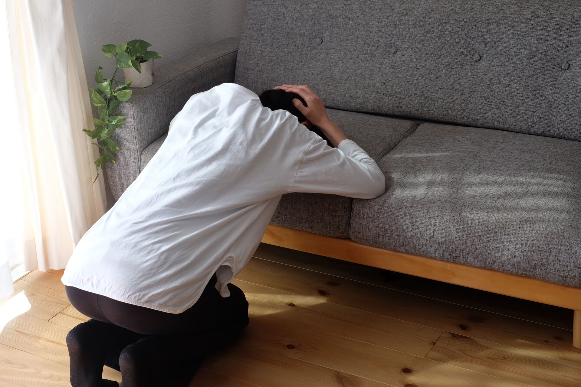 ソファに頭を預けて両手で頭を抱え、激しく後悔している人物の様子