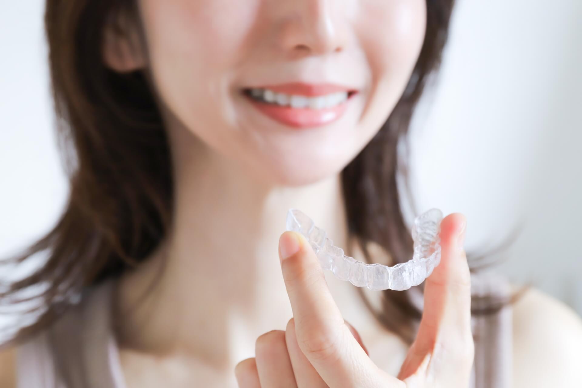 マウスピース矯正器具のアライナーを持つ女性の口元アップ