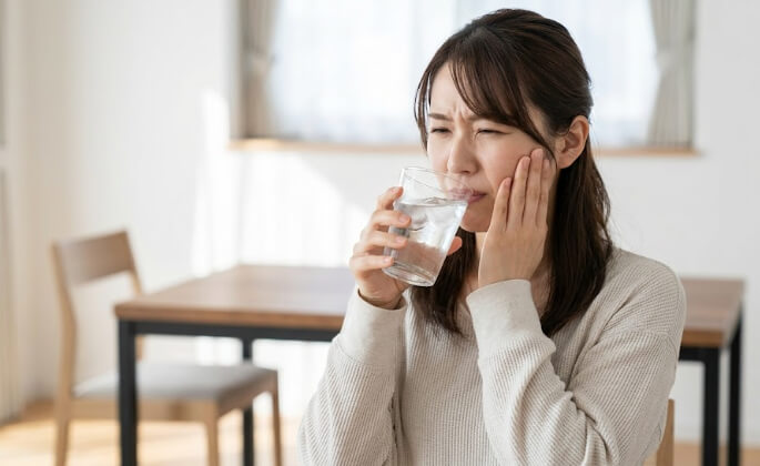明るいダイニングで、冷たい水がしみて痛がる日本人女性の実写画像。