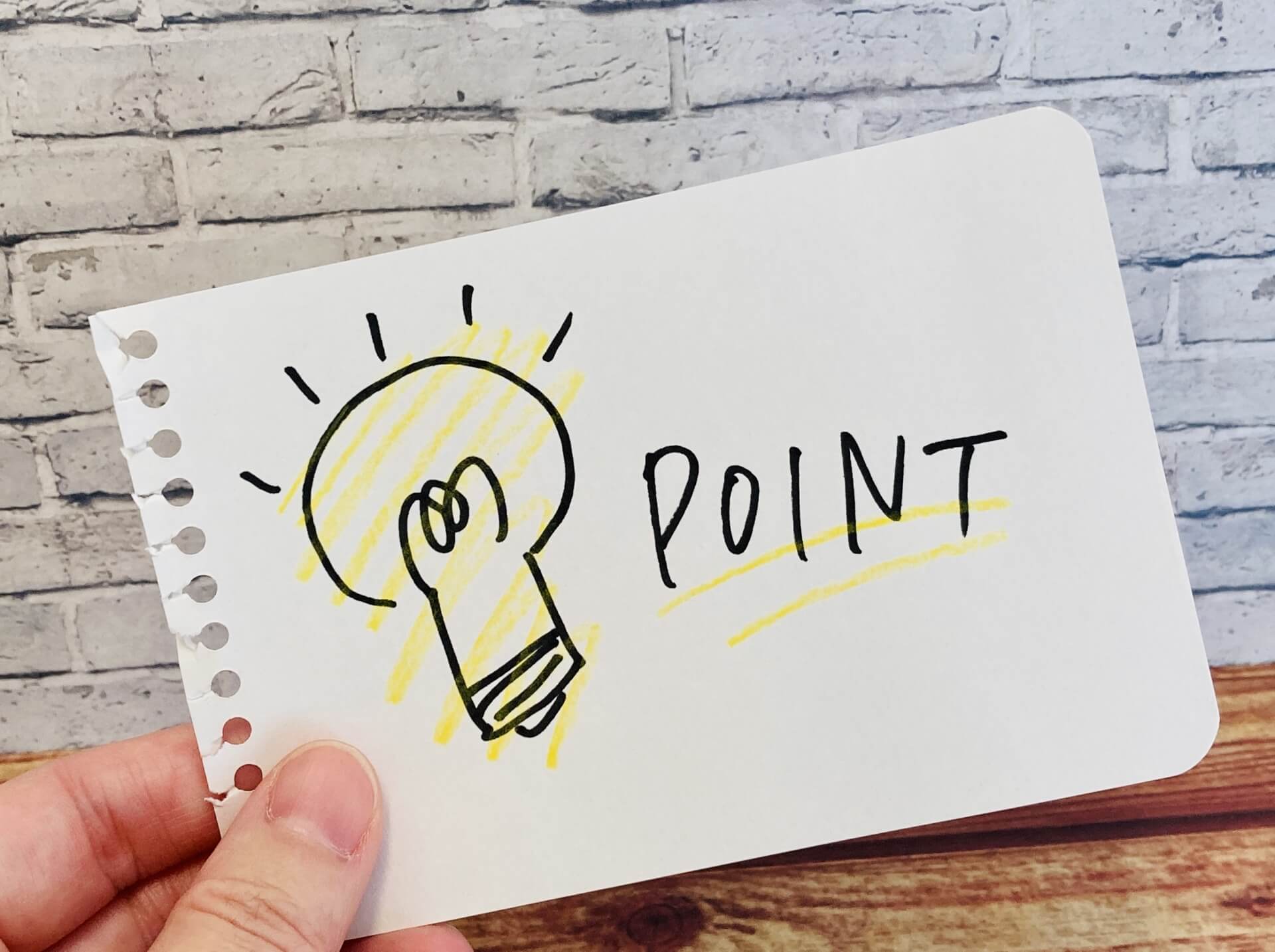 電球のイラストと「POINT」の文字が手書きされたメモ用紙を持つ手