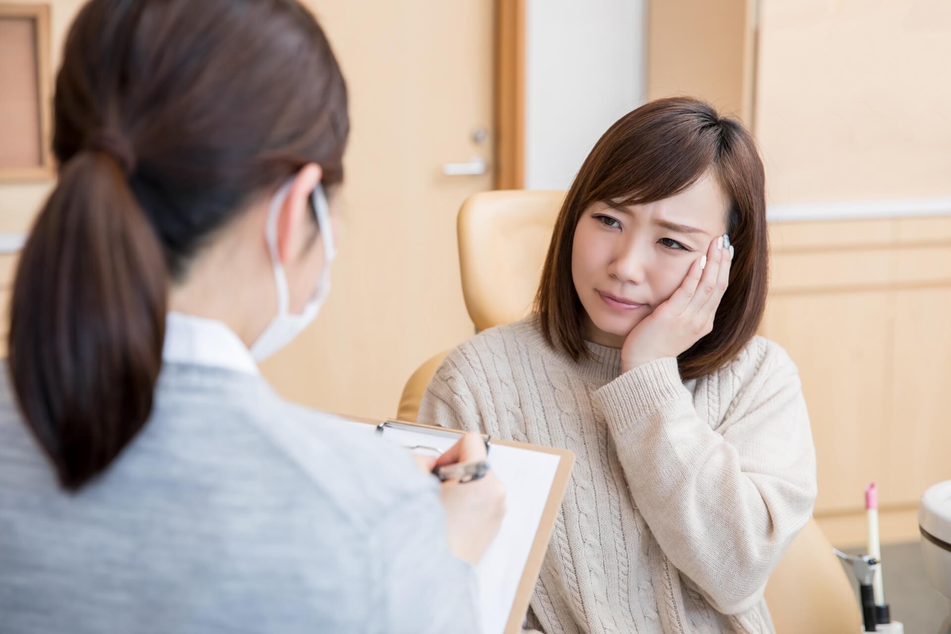 歯科医院で頬に手を当て、矯正治療に伴う痛みの不安を相談する女性の様子