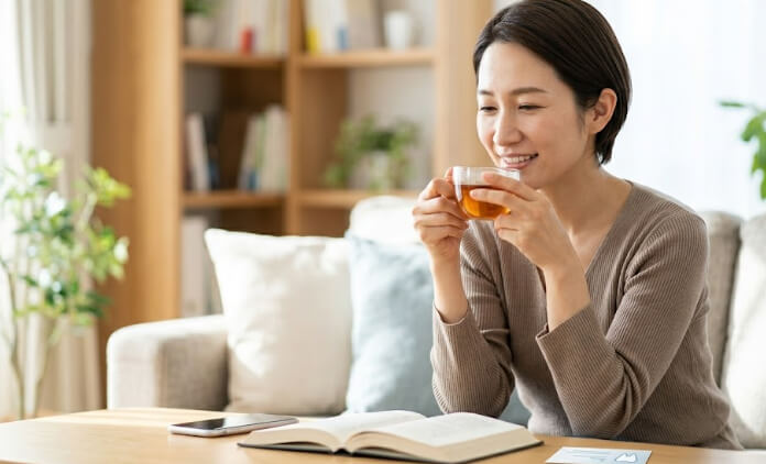 リビングで温かいお茶を飲みながら、歯の悩みから解放され、笑顔でリラックスしてくつろぐ日本人女性。