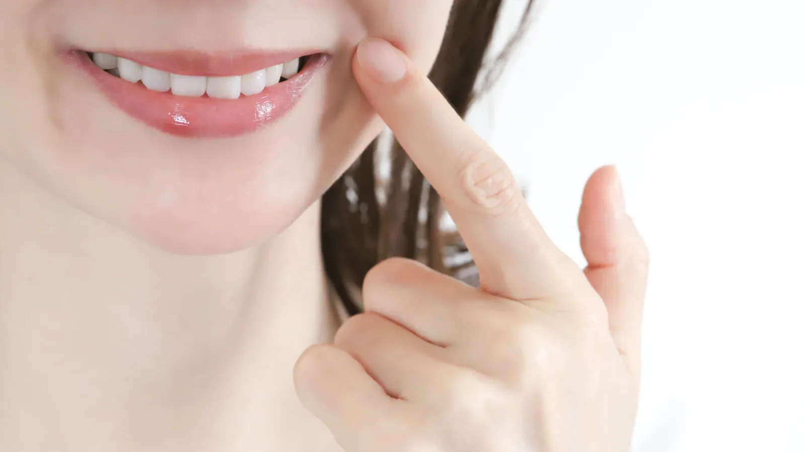 指で頬を押さえて自分の歯を気にする女性の口元（虫歯が怖くて受診をためらう場面）