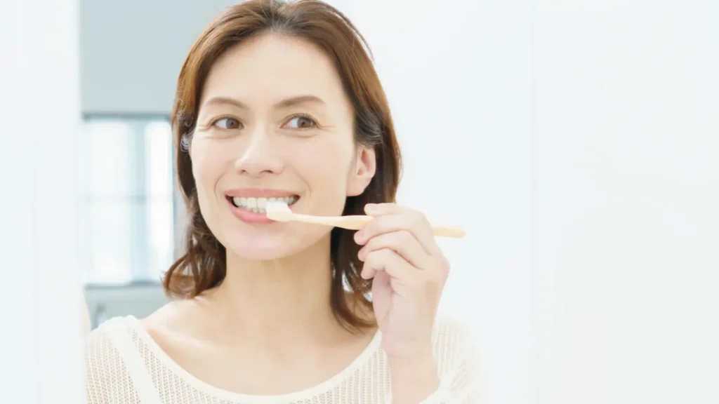 洗面所で歯ブラシを口に当てて歯を磨く女性（歯石取りと歯ぐきのケア）
