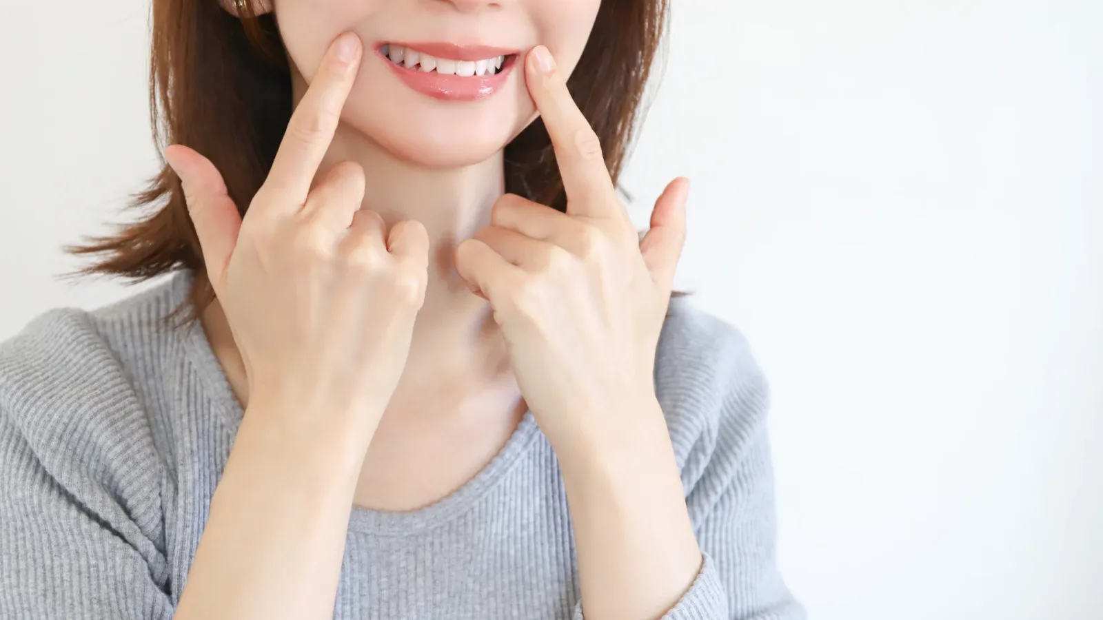 両手の指で頬を広げて自分の前歯と口元を見せる女性
